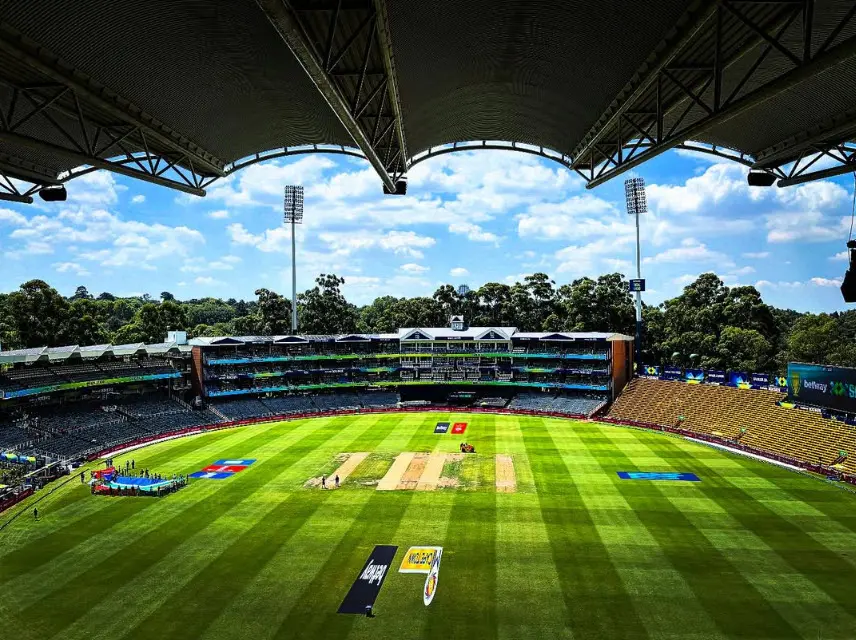 An empty cricket ground, covered grandstand and floodlights over a green pitch